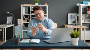 Person sits at a modern desk, looking stressed with their head in their hands, surrounded by large stacks of documents and...