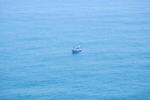 Angler on an offshore charter boat, rod bent dramatically, fighting a large fish in the deep blue sea.