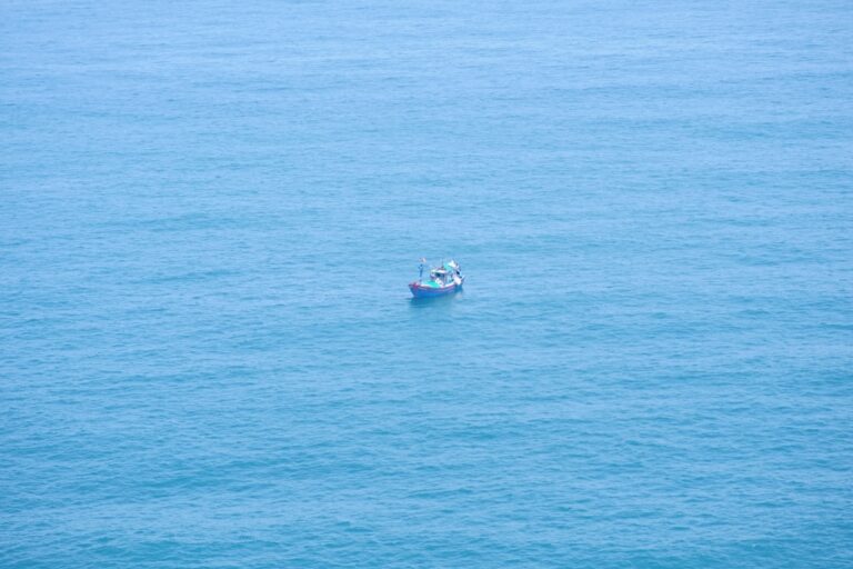 Angler on an offshore charter boat, rod bent dramatically, fighting a large fish in the deep blue sea.