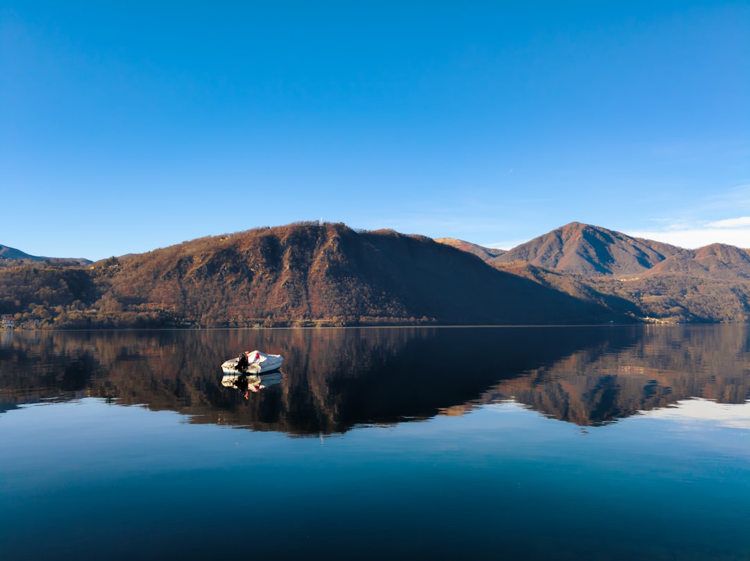 A sleek motorboat cruises across a calm, glassy lake during a serene golden hour, with the warm light of the setting sun reflecting on the water.