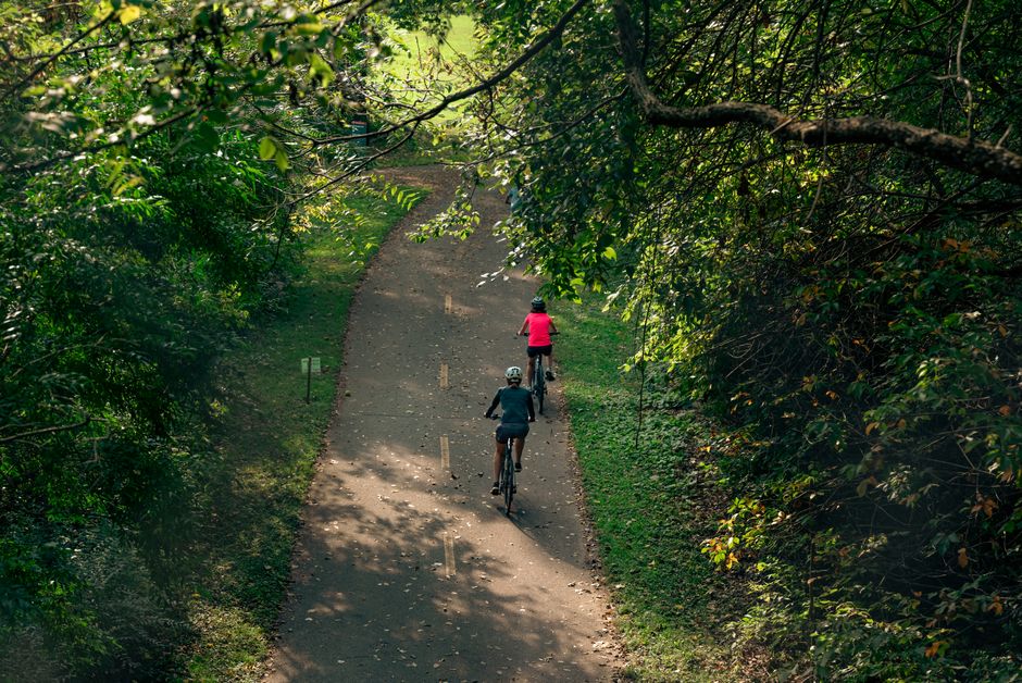 A beautiful, well-maintained riverfront park with a paved path for walking and biking alongside a wide river, showcasing community and recreational amenities.