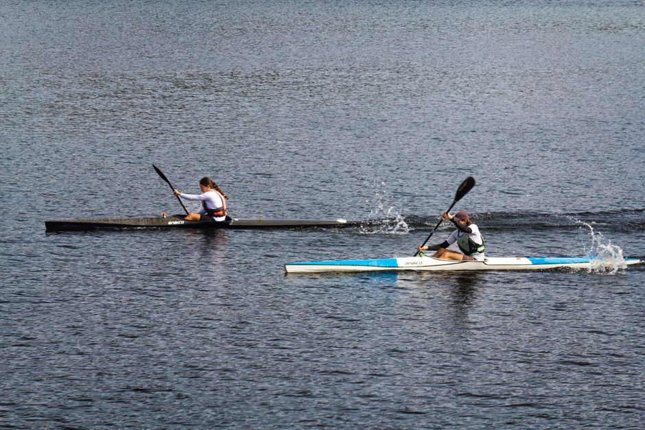 A focused athlete meticulously prepares their kayak and gear on a quiet shoreline, representing the deliberate off-water preparation needed to prevent skill atrophy.