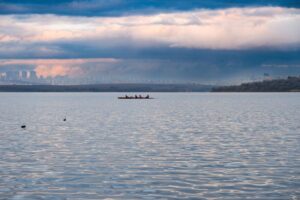 Lone rower in a scull pauses on calm, glassy water during an atmospheric sunrise, conveying a sense of introspection and a...