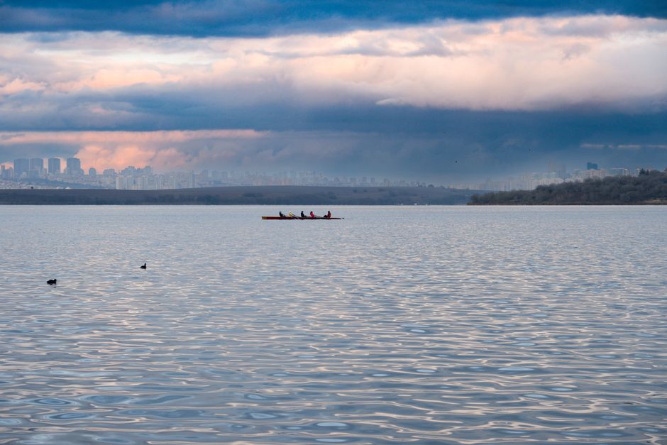 Lone rower in a scull pauses on calm, glassy water during an atmospheric sunrise, conveying a sense of introspection and a...