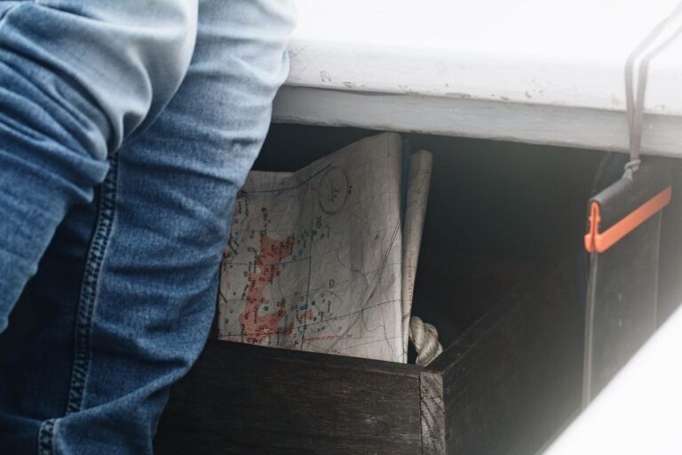 Old, weathered paper map rests on a sunny wooden dock next to calm blue water, symbolizing outdated navigation in the Colu...